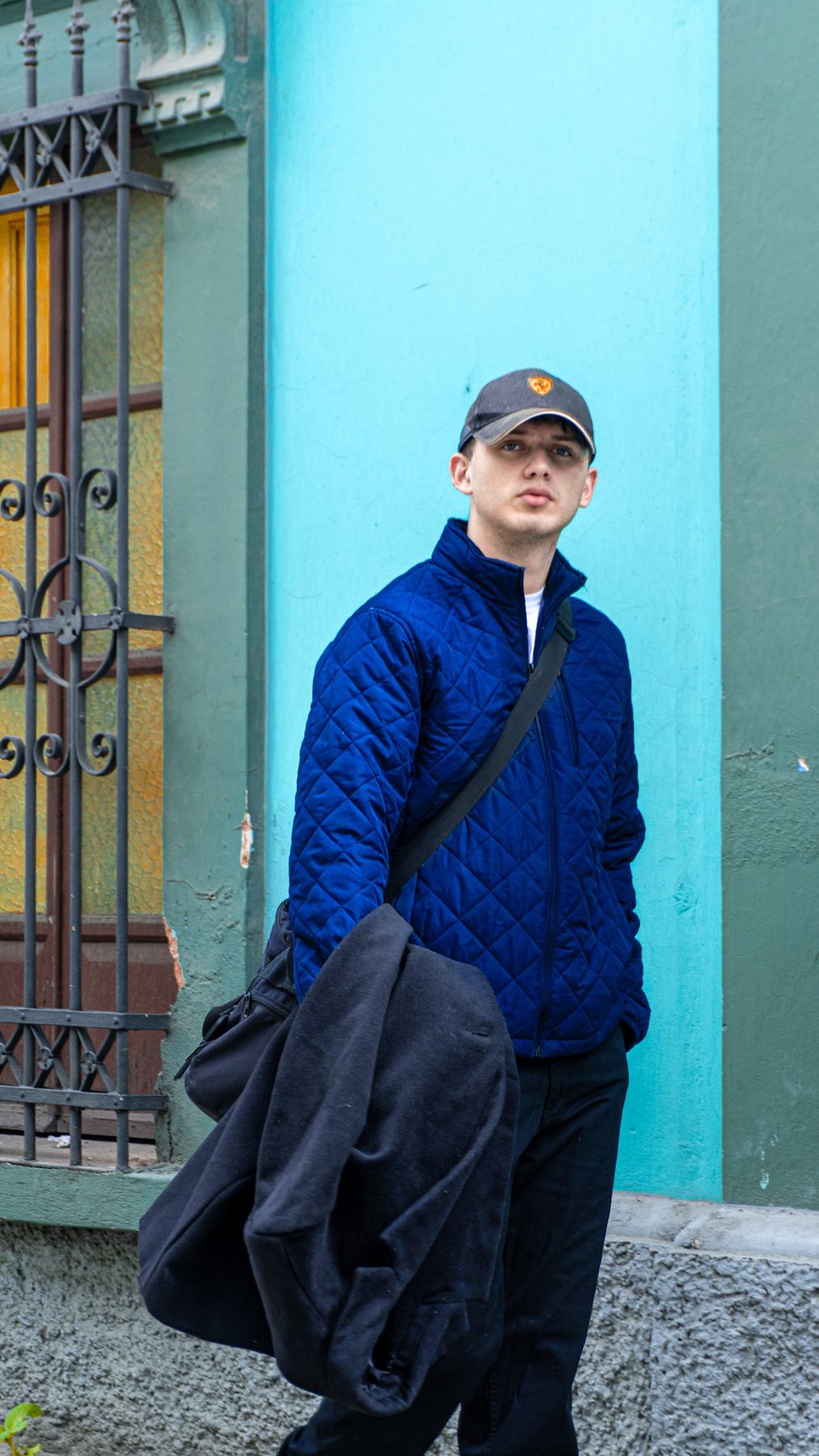 Modelo con chaqueta azul frente a fachada turquesa