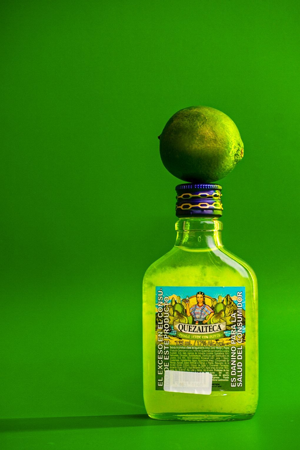 Botella verde con un limón encima sobre fondo verde